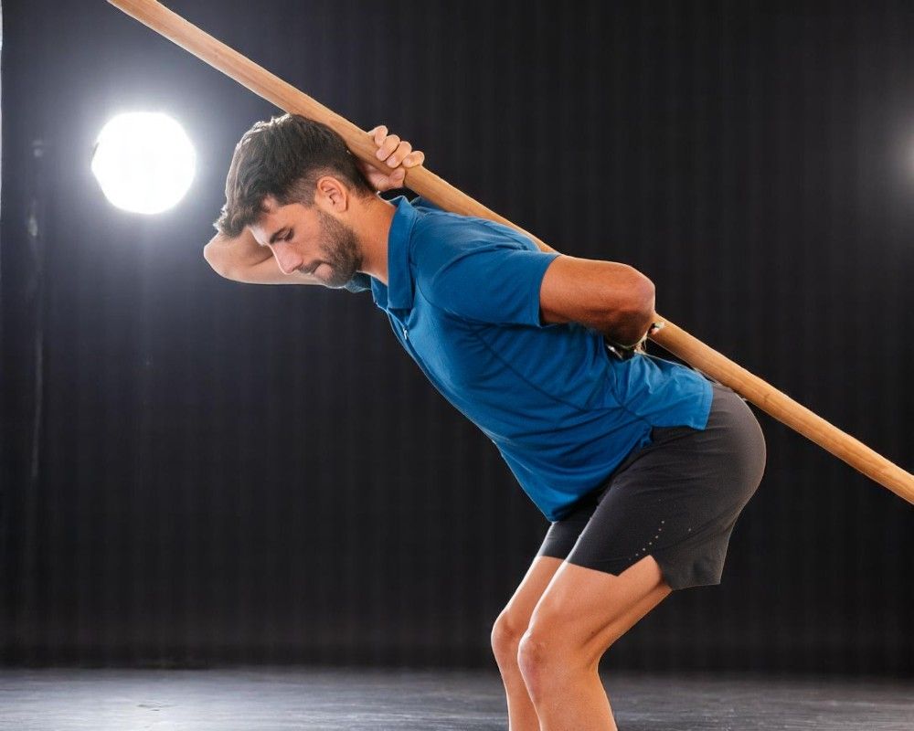 Chico con palo de madera para obligar a mantener la espalda recta. Ejercicio de reacondicionamiento postural.